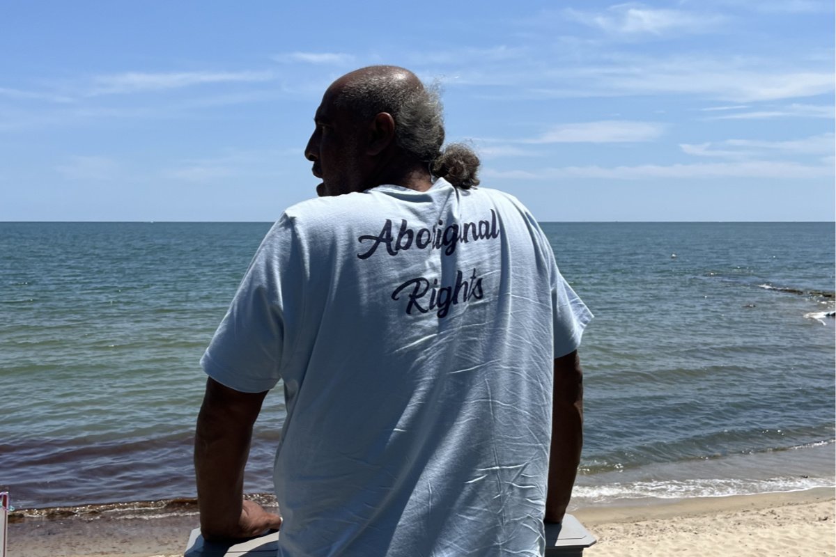 A member of the Wampanoag tribe wearing a baby blue t-shirt that says Aboriginal Rights