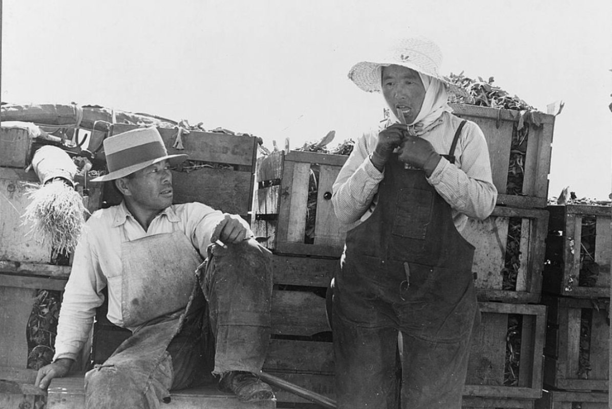 A black and white photo of Japanese American farm workers in California circa 1937. They are donning big hats and resting.