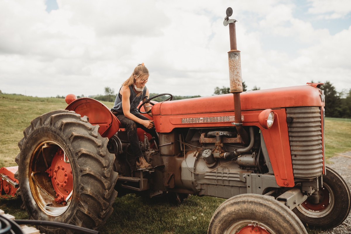 A woman with blonde hair sits on a bright red tractor in a field