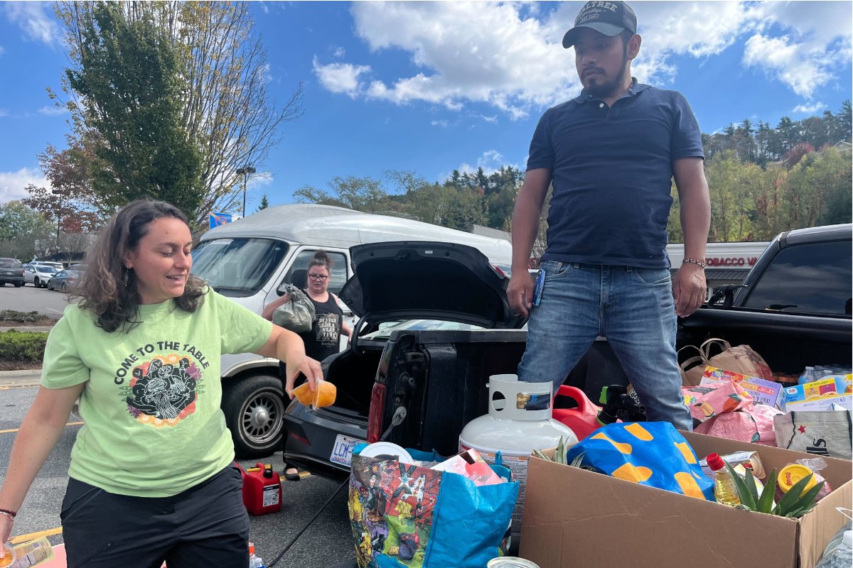 A woman stands next to a pickup truck while a young man stands on top of truck filled with canned goods, bags of food