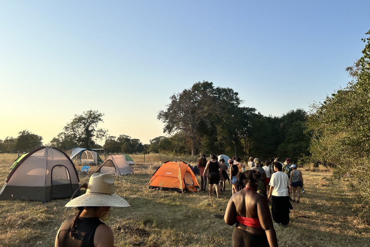 A group of BIPOC young farmers walking away from camera with colorful tents in the background of a farmland