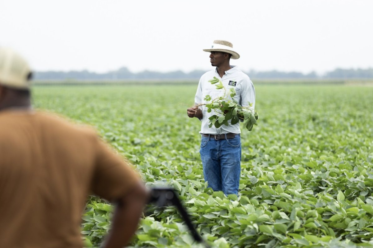 An African American farmer wearing a cowboy hat stands in a farm field